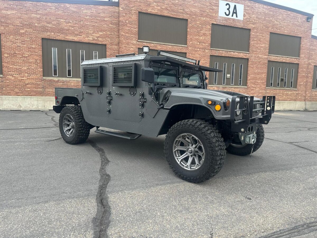 Armored Hummer H1 parked outdoors with reinforced bulletproof body panels, grated side windows, and rugged off-road tires, armored security vehicle designed for high-protection transport.